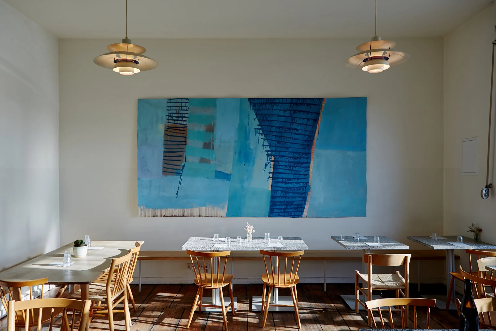 Annelies — Dining tables beneath a large blue painting